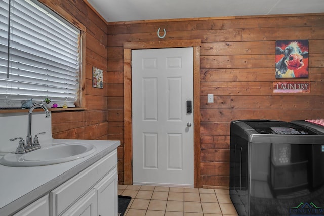 washroom with light tile patterned floors, wood walls, a sink, washer / dryer, and cabinet space