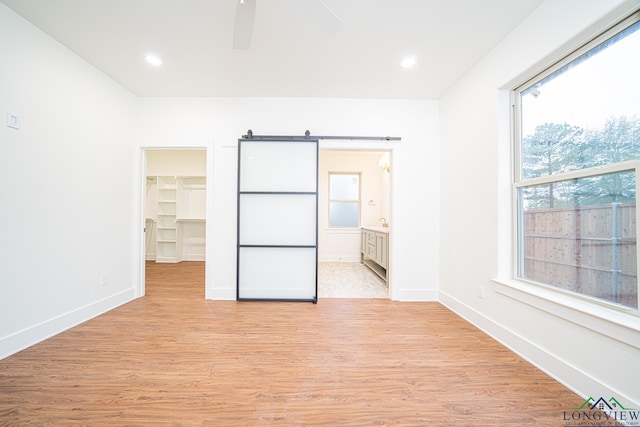 unfurnished bedroom featuring light hardwood / wood-style floors, ceiling fan, a barn door, and a spacious closet