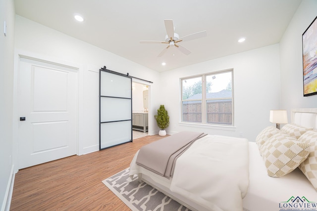 bedroom with light wood-type flooring, a barn door, ceiling fan, and connected bathroom