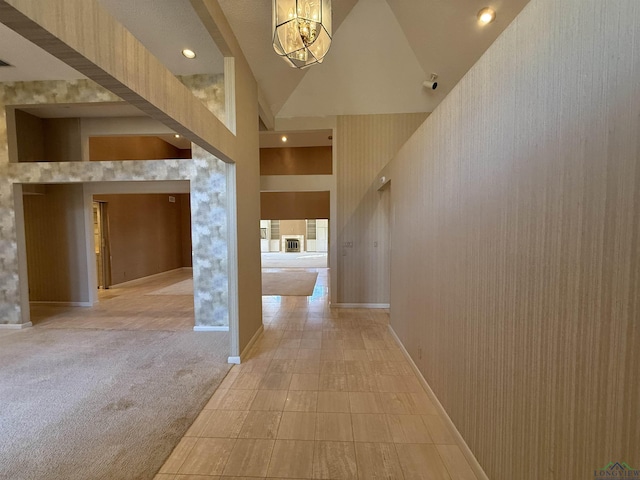 hall featuring high vaulted ceiling, light colored carpet, and an inviting chandelier