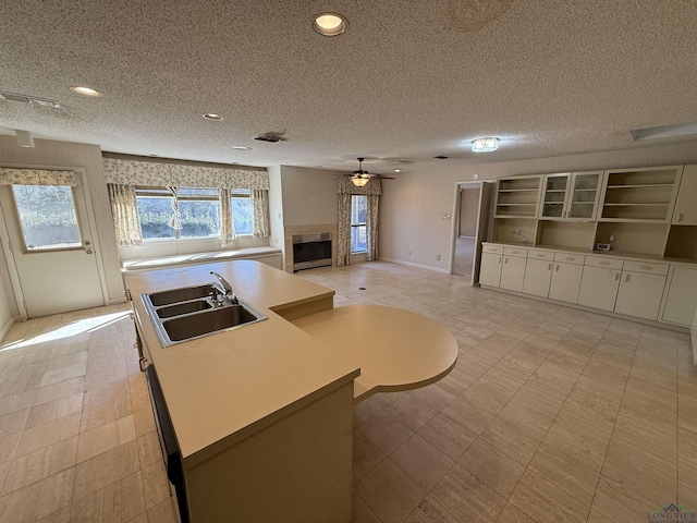 kitchen with sink, a textured ceiling, ceiling fan, white cabinets, and an island with sink