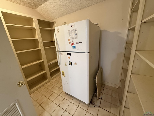 interior space featuring light tile patterned flooring, white refrigerator, a textured ceiling, and lofted ceiling