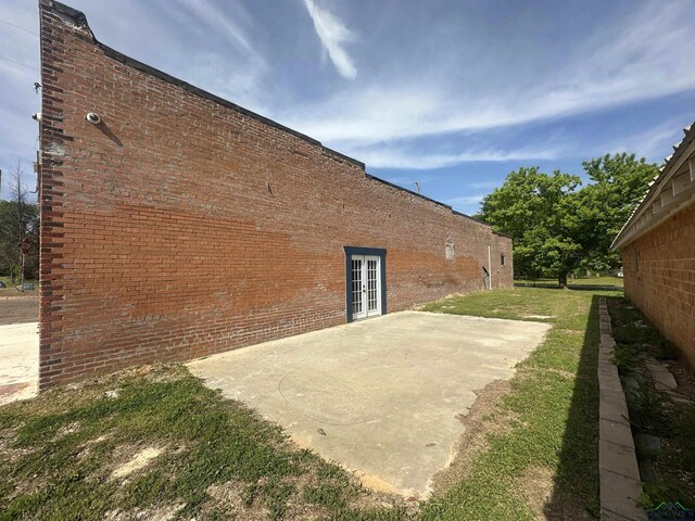 view of side of property with a patio, a lawn, french doors, and brick siding