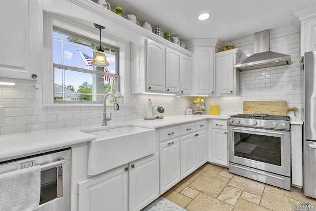 kitchen featuring stainless steel appliances, a sink, wall chimney exhaust hood, and tasteful backsplash