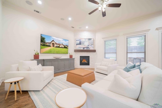 living room featuring light wood-style flooring, a ceiling fan, a fireplace, crown molding, and visible vents