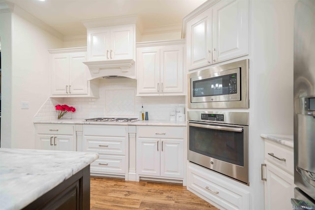 kitchen featuring light wood finished floors, decorative backsplash, white cabinetry, appliances with stainless steel finishes, and premium range hood