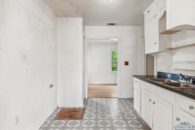 kitchen with open shelves, dark countertops, light floors, white cabinets, and a sink