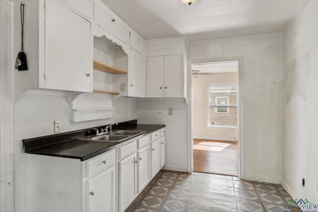 kitchen with open shelves, dark countertops, light floors, white cabinets, and a sink