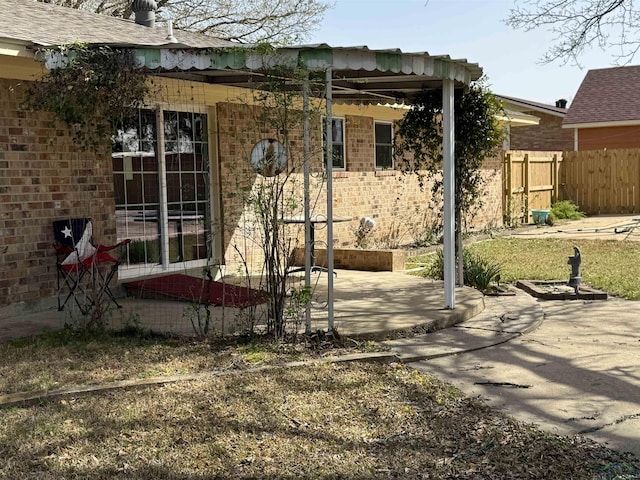 rear view of house featuring brick siding, a patio, and fence