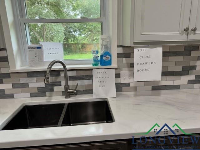 interior details featuring backsplash, white cabinets, light stone countertops, and a sink