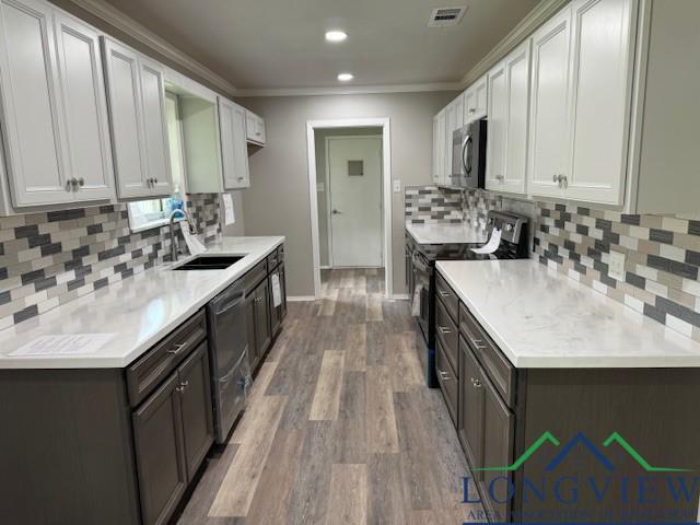 kitchen featuring sink, ornamental molding, appliances with stainless steel finishes, white cabinets, and hardwood / wood-style flooring