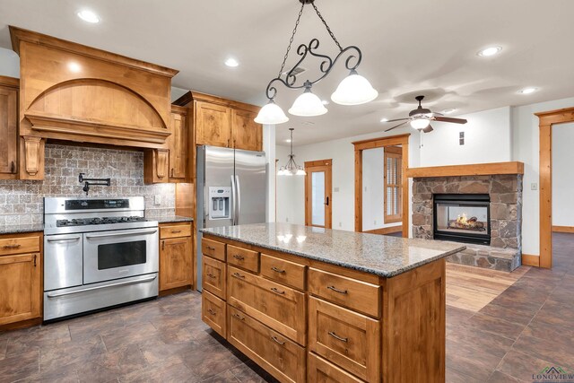 kitchen with ceiling fan, hanging light fixtures, a fireplace, a kitchen island, and dark stone counters