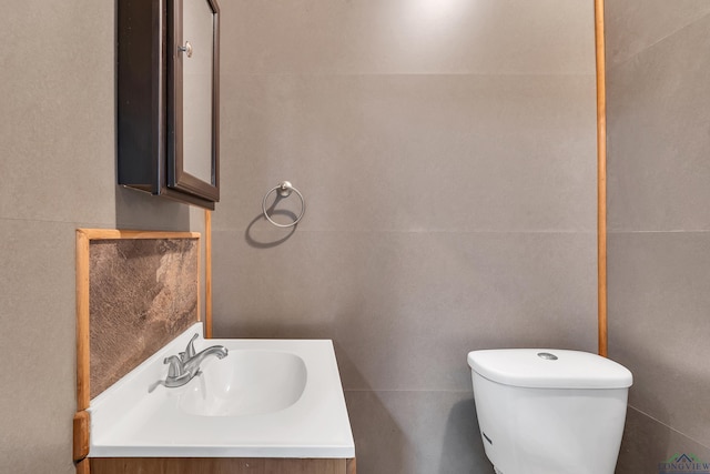 bathroom featuring vanity, tile walls, and toilet