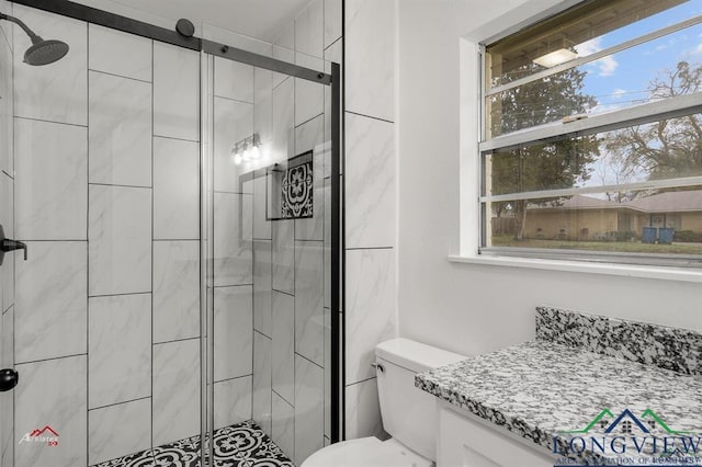 bathroom featuring a shower with shower door, toilet, vanity, and a healthy amount of sunlight