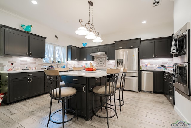 kitchen featuring hanging light fixtures, light hardwood / wood-style flooring, stainless steel fridge, a kitchen island, and a breakfast bar area