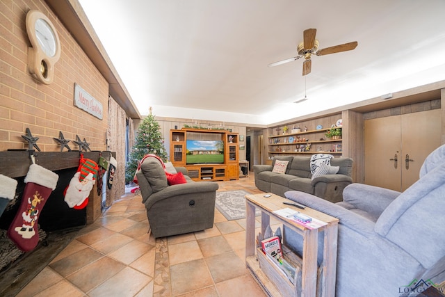 living room featuring built in shelves, ceiling fan, and brick wall