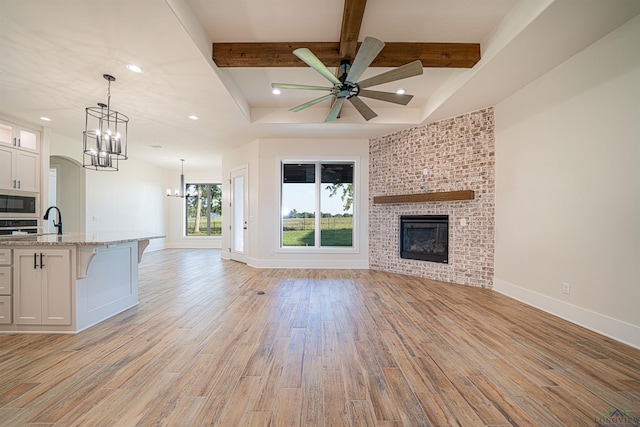 unfurnished living room with sink, light hardwood / wood-style flooring, ceiling fan, a fireplace, and beam ceiling