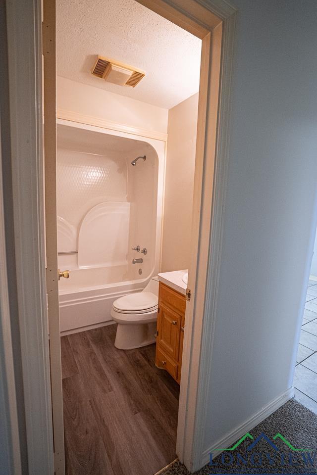 full bathroom with shower / bathtub combination, a textured ceiling, vanity, hardwood / wood-style flooring, and toilet