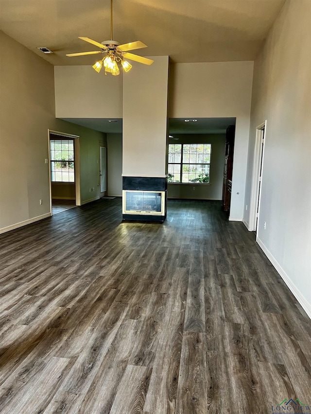 unfurnished living room featuring ceiling fan, dark hardwood / wood-style flooring, and a towering ceiling