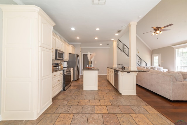 kitchen featuring ornate columns, ceiling fan, stainless steel appliances, a center island with sink, and ornamental molding