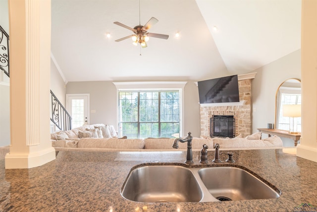 kitchen featuring ceiling fan, sink, dark stone counters, vaulted ceiling, and a fireplace