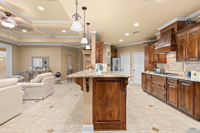 kitchen with pendant lighting, custom exhaust hood, a center island with sink, appliances with stainless steel finishes, and light stone counters