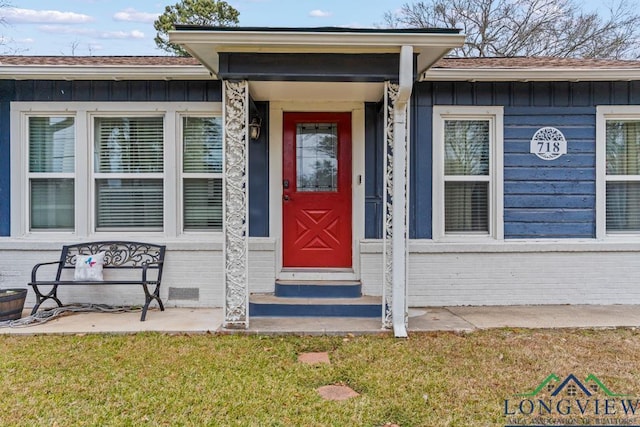 718 Pine St, Gilmer, TX 75644 - view of exterior entry with board and batten siding, brick siding, and a lawn