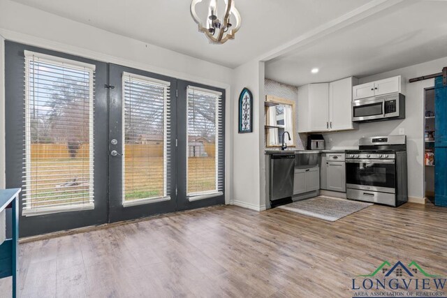 718 Pine St, Gilmer, TX 75644 - kitchen with french doors, wood finished floors, an inviting chandelier, white cabinets, and appliances with stainless steel finishes