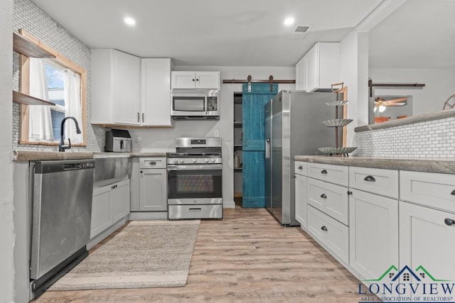 718 Pine St, Gilmer, TX 75644 - kitchen featuring light wood finished floors, white cabinetry, stainless steel appliances, and a barn door