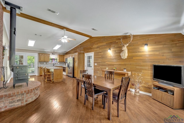 dining room featuring ceiling fan, a wood stove, light hardwood / wood-style flooring, and lofted ceiling with skylight