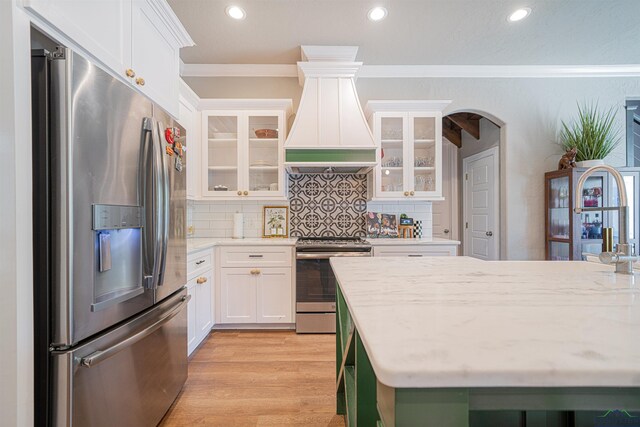 kitchen featuring backsplash, premium range hood, crown molding, appliances with stainless steel finishes, and white cabinetry