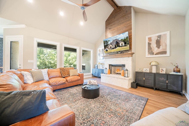 living room featuring beam ceiling, ceiling fan, a stone fireplace, high vaulted ceiling, and light hardwood / wood-style floors