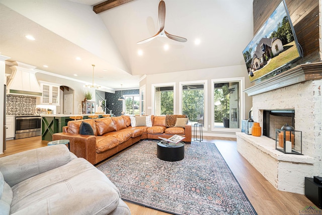 living room with beam ceiling, ceiling fan, a stone fireplace, high vaulted ceiling, and light wood-type flooring