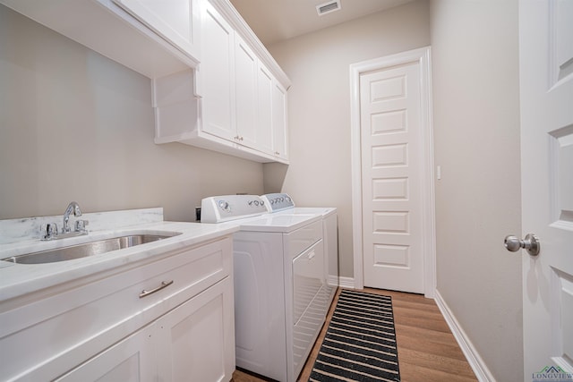 clothes washing area with washer and dryer, light hardwood / wood-style floors, cabinets, and sink