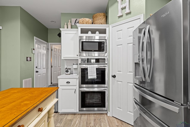 kitchen with stainless steel appliances, white cabinetry, and light wood-type flooring