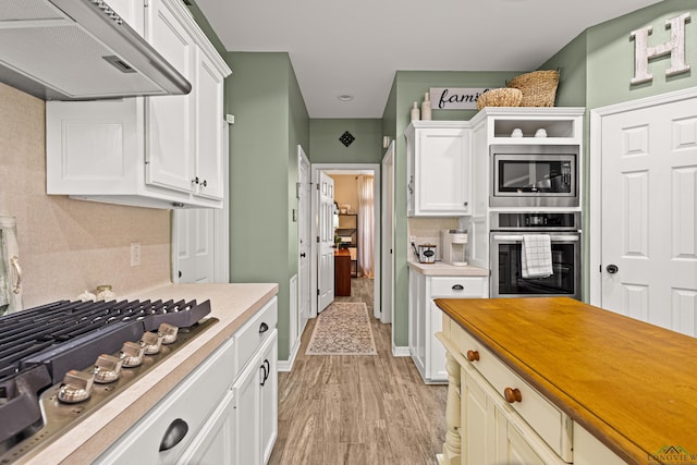 kitchen featuring white cabinets, light wood-type flooring, appliances with stainless steel finishes, and tasteful backsplash