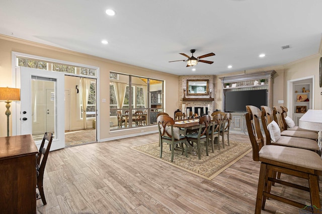 dining room featuring wood-type flooring, a fireplace, ornamental molding, and ceiling fan