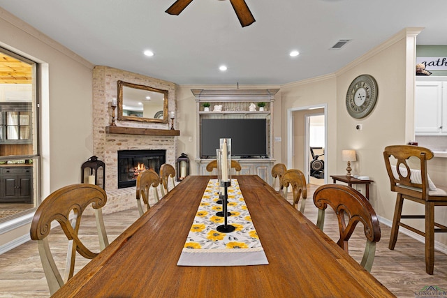 dining space with a brick fireplace, ceiling fan, ornamental molding, and light hardwood / wood-style flooring