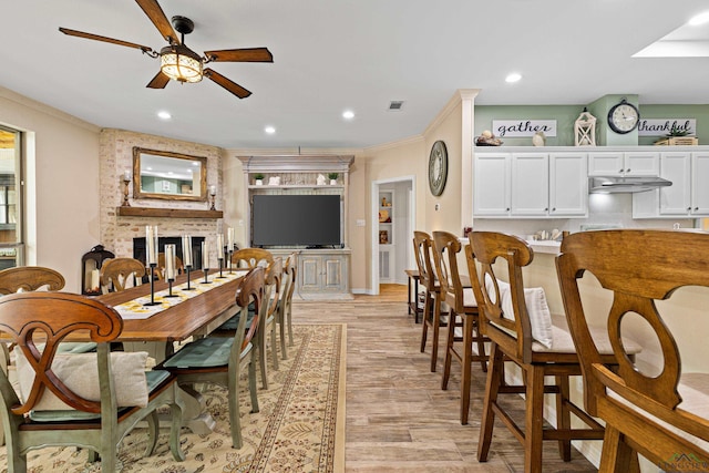 dining space with a fireplace, light wood-type flooring, ceiling fan, and crown molding