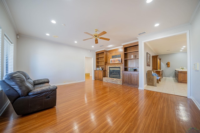 living room with a fireplace, light hardwood / wood-style floors, ceiling fan, and crown molding