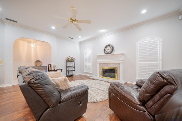 living room with hardwood / wood-style flooring, ceiling fan, ornamental molding, and a fireplace