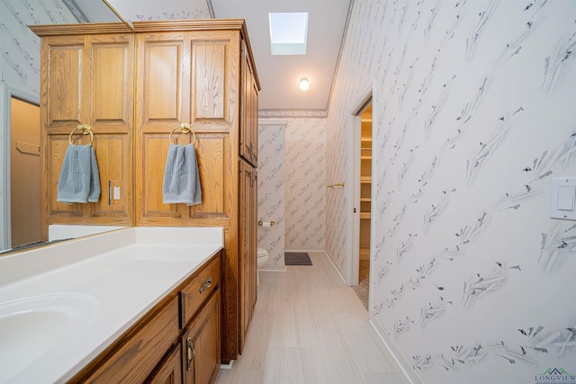 bathroom featuring vanity, toilet, crown molding, and a skylight