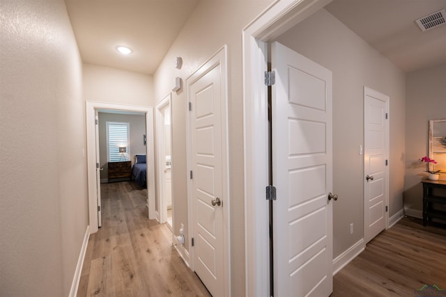 corridor with light wood finished floors, baseboards, and visible vents