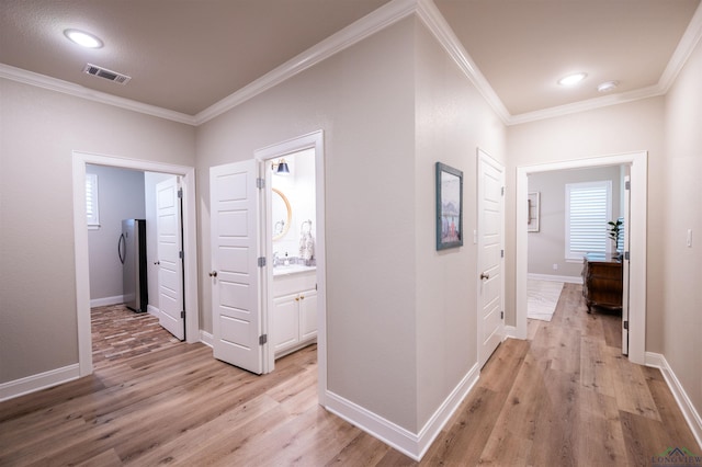 hallway with light wood-style flooring, ornamental molding, and baseboards