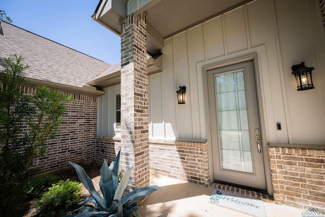 view of exterior entry with roof with shingles, board and batten siding, and brick siding