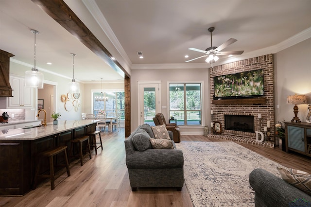 living room featuring light wood-style flooring, a fireplace, crown molding, and ceiling fan with notable chandelier