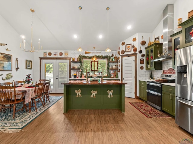 kitchen with a center island with sink, vaulted ceiling, decorative backsplash, wall chimney exhaust hood, and appliances with stainless steel finishes