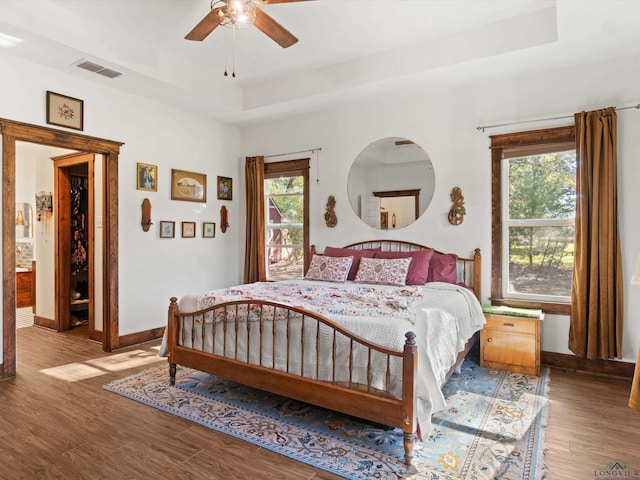 bedroom with multiple windows, wood-type flooring, a tray ceiling, and ceiling fan