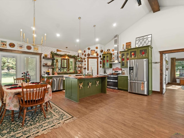 kitchen featuring wall chimney exhaust hood, stainless steel appliances, decorative light fixtures, a center island, and green cabinets