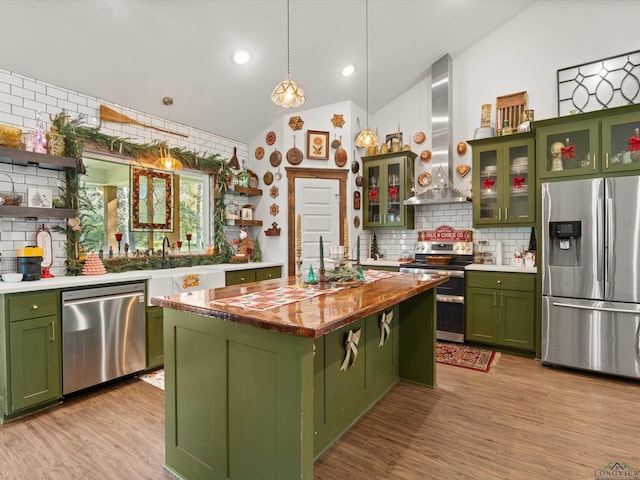 kitchen with lofted ceiling, wall chimney range hood, appliances with stainless steel finishes, tasteful backsplash, and a kitchen island